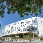 The curved, hexagon-patterned facade of Calgary's Central Library framed by trees under a blue sky