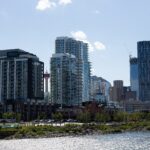 Modern condominium towers in Calgary's East Village beside the river, with The Bow and the Calgary Tower behind