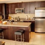 Kitchen with dark wood cabinets, stainless steel appliances and an island with bar stools in a Calgary townhome