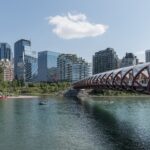 The red helix-shaped Peace Bridge spanning the Bow River in front of downtown Calgary's Eau Claire high-rises on a sunny summer day