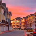 Rows of three-storey townhouses with front garages under a pink and orange sunset sky in West Springs, Calgary